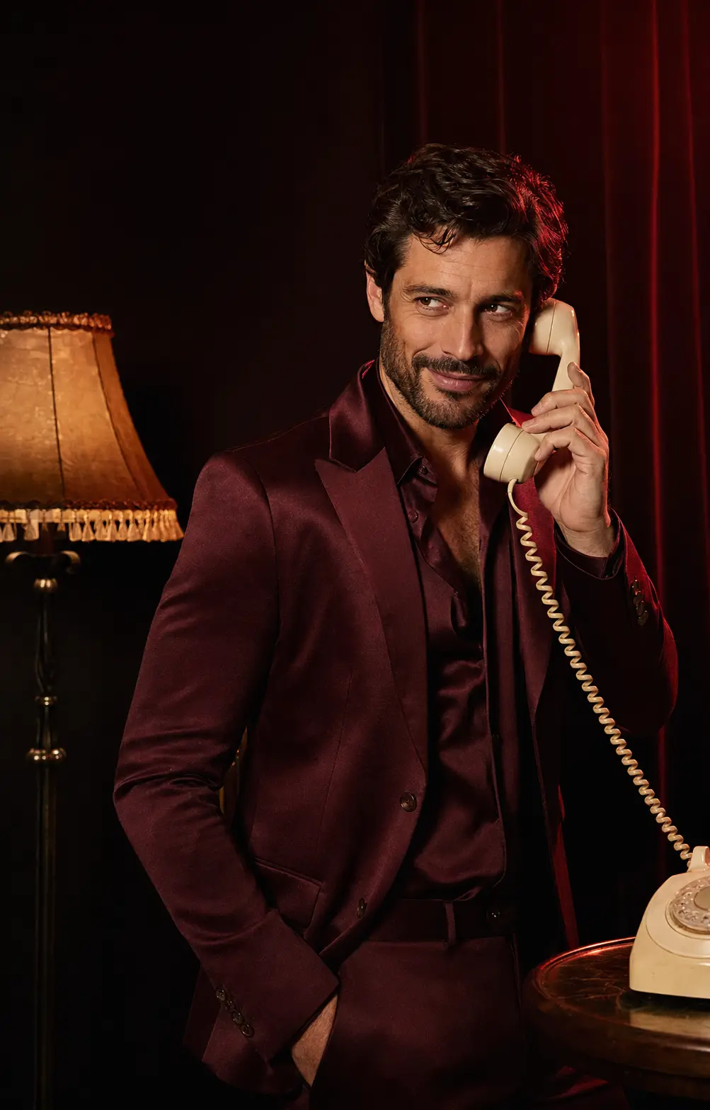 Sam, homme adulte en costume bordeaux, souriant avec un téléphone vintage